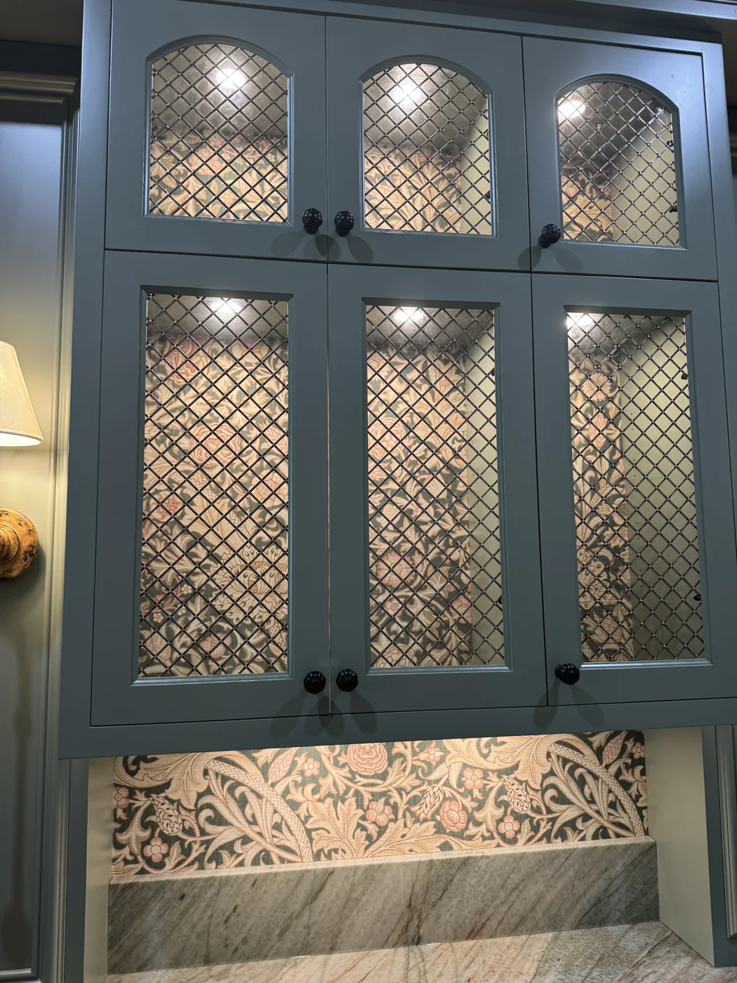 Patterned wallpaper installed behind blue glass-front display cabinets