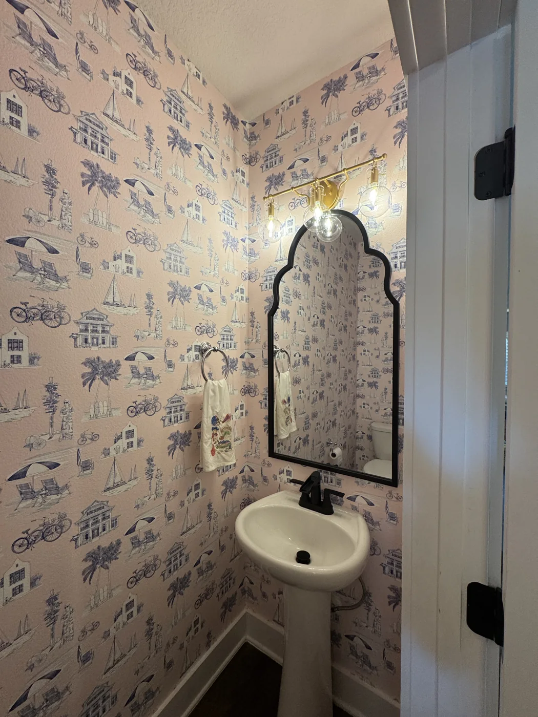 Pink coastal toile wallpaper surrounding a finished powder room