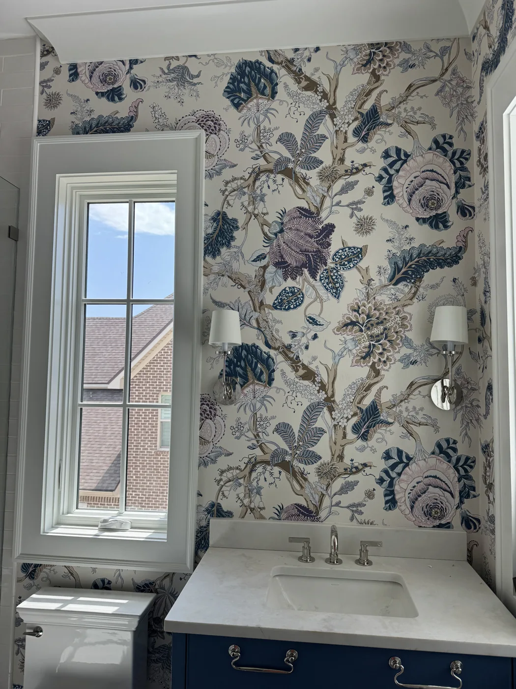 Blue and violet botanical wallpaper installed around a powder room window and vanity