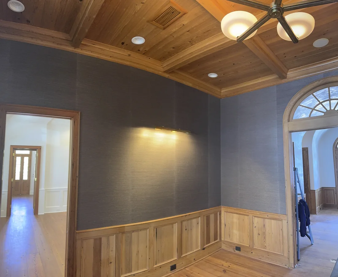 Textured dark grasscloth walls framed by natural wood paneling and ceiling beams